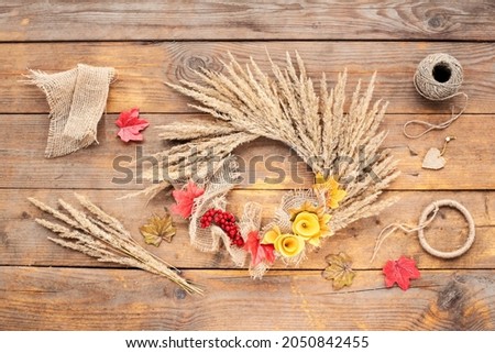 Dried floral wreath, autumn rustic wreath with dry grass, wildflowers  on rustic wooden table. Floral autumn door wreath from natural materials. Fall flower decoration workshop. Top view