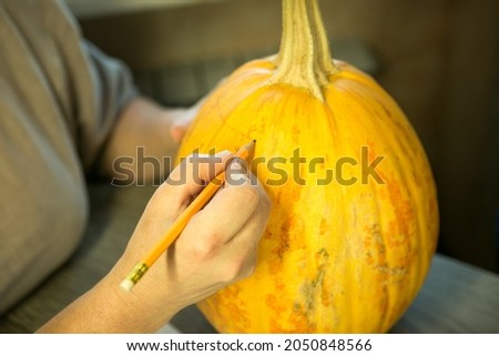 Making Jack O'Lantern at home. A female hand with a pencil marks the cut lines on the pumpkin.