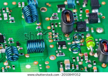 Electronic components to receiving radio-frequency signal on green printed circuit board. Planar spiral coil in PCB layer, air-core inductors and surface-mount devices inside RF module of TV receiver. Royalty-Free Stock Photo #2050849352