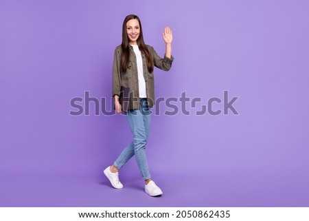 Full size profile side photo of cheerful lovely female go walk hold laptop say hello isolated on violet color background