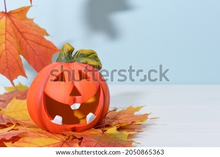Smiling ceramic pumpkin lantern on a blue background with autumn maple leaves. Happy Halloween or Thanksgiving concept with copy space. Funny Jack'o'lantern as a symbol of autumn and harvest.