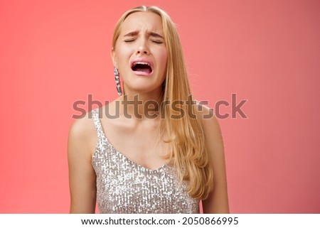 Immature whining spoiled adult rich daughter blond long hair in silver stylish dress complaining sad cruel unfair life crying sobbing frowning sulking upset, standing disappointed red background Royalty-Free Stock Photo #2050866995