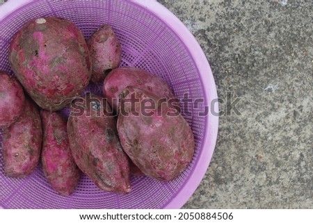 a few red sweet potatoes in a purple basket lying on the cor floor