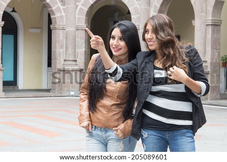 two latin girls smiling and pointing at a place