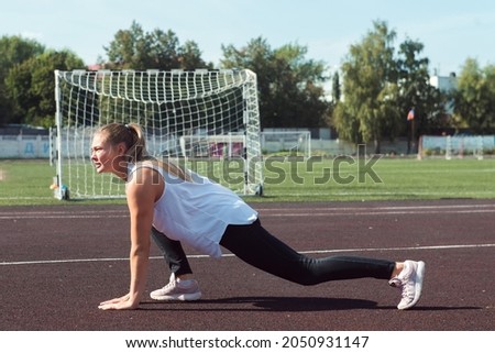 Young sporty woman doing lunges exercises at stadium
