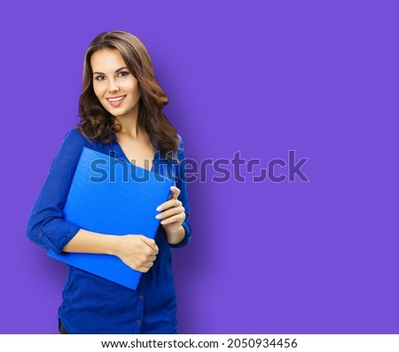 Portrait of happy smiling young brunette woman in blue confident wear with folder, isolated on violet purple color background. Business studio concept. Copy space blank area for text. Female executive