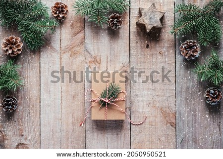 Christmas gift box wrapped in kraft paper with Christmas tree branch on wooden background, Christmas frame with fir tree branches, pine cones and candle star on wooden background