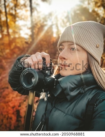 Selfie portrait of young woman in autumn park holding camera and photographing landscape.