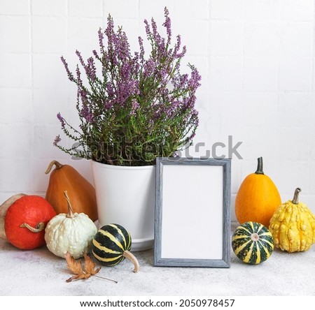 Picture frame and pumpkin decor on the table over white tile background. Fall season greeting card.