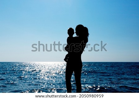 A young girl holds a child in her arms against the sun. Silhouette photography. High quality photo