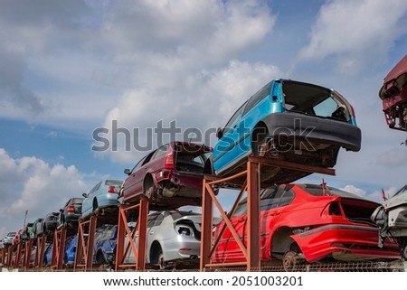 Stacked cars on a metallic frame, used for parts. Scrapyard perspective with blue skies and fluffy clouds. A lot of copy space Royalty-Free Stock Photo #2051003201