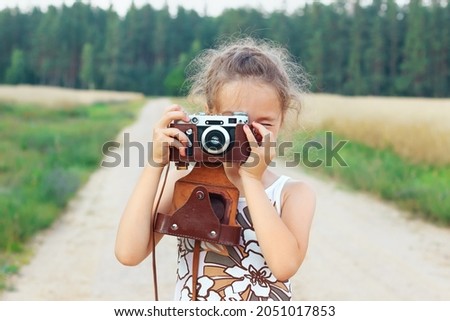 Happy beautiful  little girl in retro outfit  is taking pictures with old film camera.