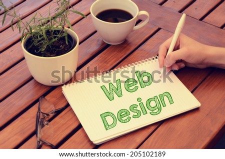 Woman hand writing in notebook Web Design on wooden table with coffee, plant and glasses. Retro colors.