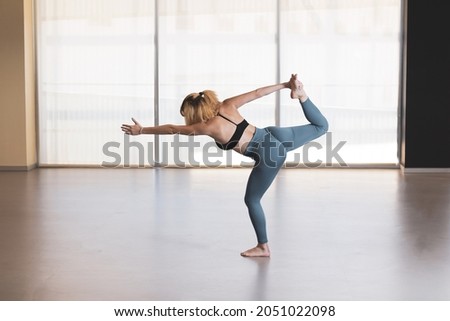 Beautiful young woman practicing yoga by the window of a gym room. Harmony, balance, meditation, relaxation, healthy lifestyle concept
