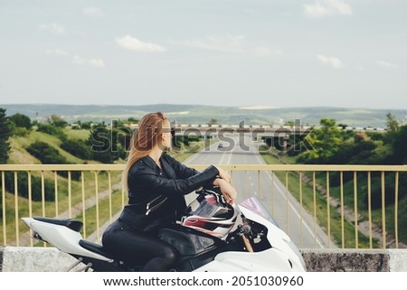 Young woman resting on a motorbike while looking over bridge on the road. Security on the roads, helmet, gloves for bikers. Biker dreaming to new destinations to travel, profile picture.