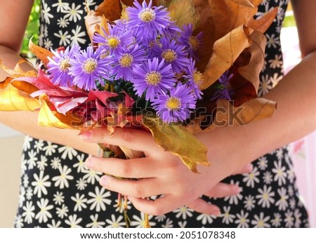 Girl hold a bunch of autumn leaves and purple flower in her hands