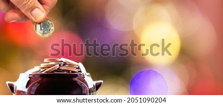 Hand putting money in coin pot and colorful background with bokeh lights.