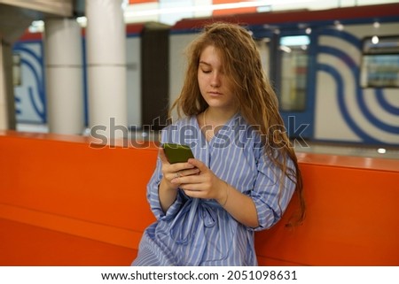 A woman using a smartphone in a modern subway. Hipster girl with a cell phone in her hand waiting on the platform of a railway station for train to arrive. Public transport.