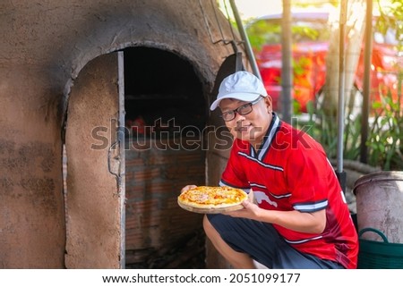 Man wearing red shirt and white hat holding homemade pizza.