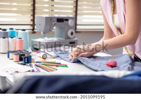 Portrait of a young, attractive woman on a stylish fashion designer's table, surrounded by color textile samples. Attractive woman working in a fashion studio with mannequins and colorful cloths.