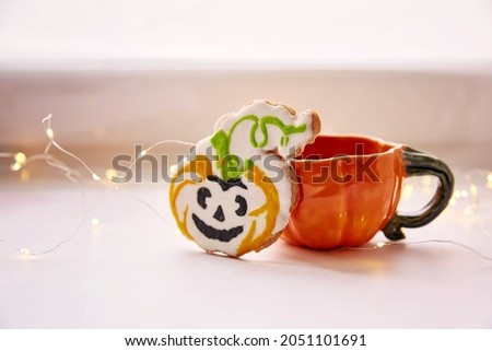 Halloween cookies. Pumpkin cup and homemade cookies in shape of cute pumpkins. Atmospheric aesthetic autumn mood or trick or treat concept. Copy space. Home cooking and coziness. Close up,copy space