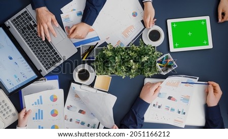 Top view of businesswoman looking at mock up green screen chroma key tablet with isolated display while company teamwork checking financial accounting graphs. Business group working in startup offce