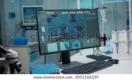Empty laboratory room with dna animation on monitor for scientific innovation. Nobody but microscope, vacutainers, test tubes and micropipette as biochemistry instruments on desk