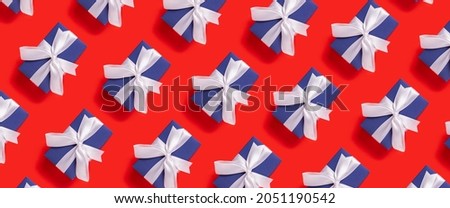 Lots of Christmas gift boxes blue with a white ribbon on a red background. Top view, flat lay. Banner.