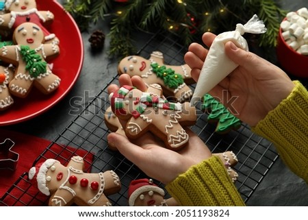 Making homemade Christmas cookies. Girl decorating gingerbread man at black table, closeup Royalty-Free Stock Photo #2051193824