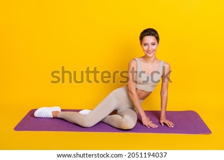 Portrait of attractive sportive cheerful girl sitting on mat work out weight loss isolated over bright yellow color background