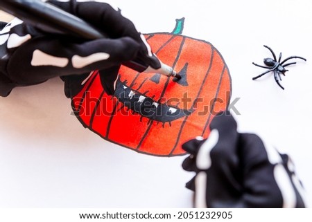 Hands drawing a toothy pumpkin for Halloween, close-up. Sketch drawing of an orange laughing pumpkin with sharp teeth. Get ready for the party. Jack Lantern.