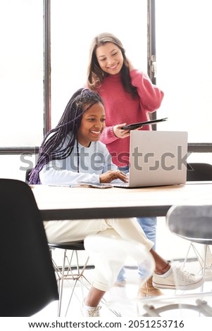 Vertical photo. In the office: two women work together. They discuss work issues amicably while looking at the computer screen.