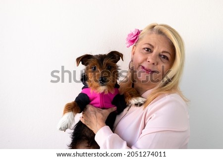 woman smiling looking forward holding a dog wearing pink outfit, dog in pink outfit, pink october