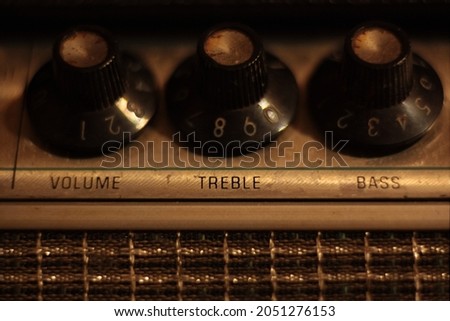 Treble, volume and bass control knobs on 1960s vintage guitar amp head. Warm color temperature, shallow depth of field, macro.
