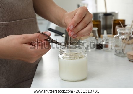 Woman cutting wick of homemade candle at table indoors, closeup Royalty-Free Stock Photo #2051313731