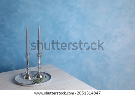 Holders with candles on wooden table near light blue wall, space for text