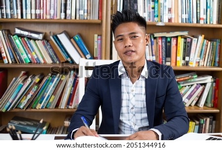 A Southeast Asian guy from Malaysia studying in a library wearing a shirt with a suit Royalty-Free Stock Photo #2051344916
