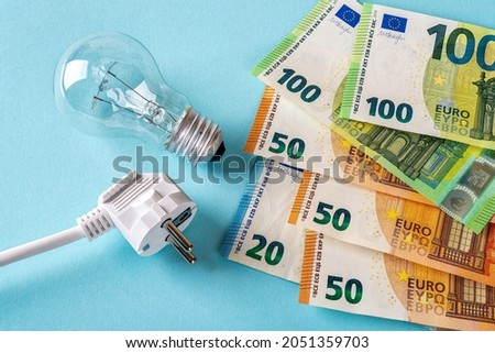 Electric plug, light bulb and euro money banknotes over blue background. Increasing of electricity cost for residential and business users, expensive energy bill and rise in electricity prices concept Royalty-Free Stock Photo #2051359703