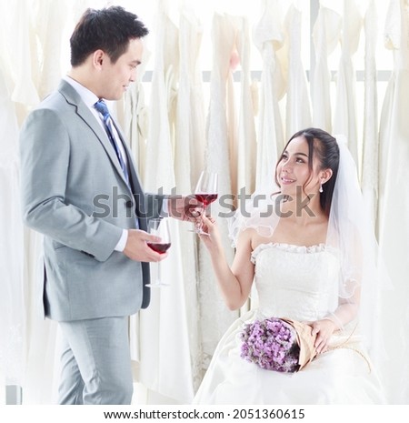 The groom in a gray suit is giving the bride a glass of wine to the bride in a white lace dress on the day of the wedding to celebrate happily. Concept love best day