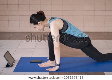 A South Asian woman in a sports outfit watching an online workout program via tablet in the home