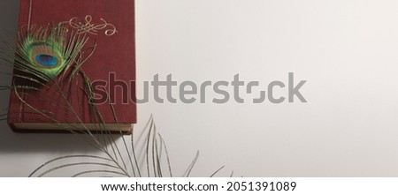 Old brown book in composition with peacock feather on white background. Card