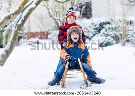 Two kid boys having fun sleigh ride during snowfall. Children sledding on snow. siblings riding a sledge. Twins play outdoors. Friends sled in snowy winter park. Active fun for family vacation