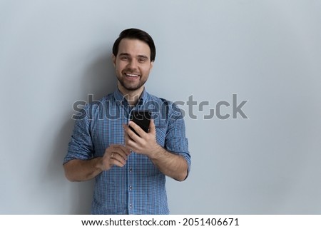 Head shot portrait smiling man holding smartphone, standing on grey studio background isolated, looking at camera, happy laughing young male having fun with mobile device, using social media