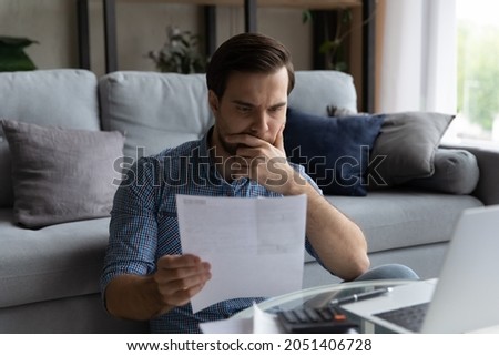 Thoughtful man checking financial documents, holding receipt, calculating domestic bills or taxes, using laptop, unhappy pensive young male touching chin, unexpected debt or bankruptcy concept Royalty-Free Stock Photo #2051406728