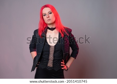 Kitsch style, fashion of the future. mixing styles. A young woman with bright scarlet hair in dark unusual clothes on a gray background