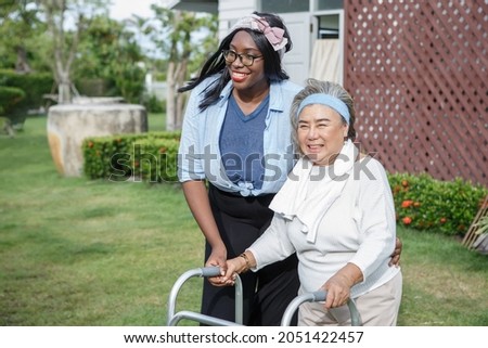asian senior mother walk with walker and african american carer support in garden at home. old woman disabled walking and black caregiver young woman helping in back yard park outdoors. health care  Royalty-Free Stock Photo #2051422457
