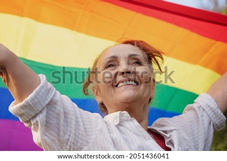 Beautiful mature woman with charming smile holding rainbow LGBT flag in her hands, gay and lesbian rights concept for all ages Royalty-Free Stock Photo #2051436041