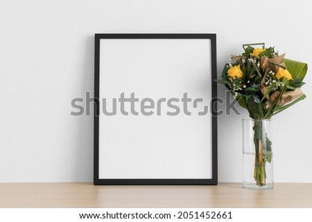 Black frame mockup with a bouquet of roses on the wooden table.