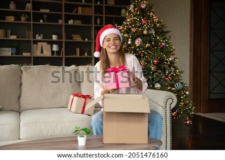 Happy woman receiving delivery box with Christmas gifts, unpacking parcel with New Year presents, holding festive wraps, unboxing received package, smiling at camera, smiling. Xmas portrait