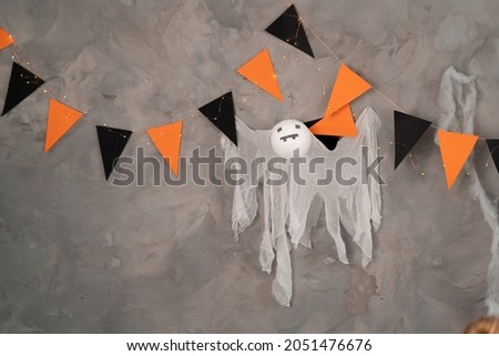Halloween festive decoration, orange black flags and ghost hanging on the concrete wall of the room interior close-up. Place for text